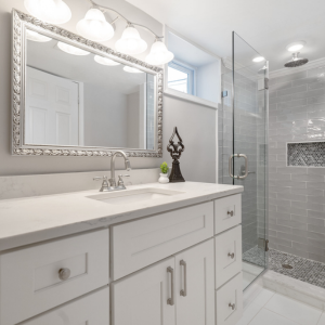 An remodeled bathroom from Veteran Built Homes in Northern Virginia. Grey shower tile with glass wall, white vanity with grey countertop and a modern light fixture.