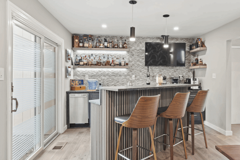 Custom basement bar remodel in Northern Virginia by Veteran Built Homes featuring modern backsplash tile, quartz countertops, wood bar stools, floating shelves with backlighting, and built-in beverage station.