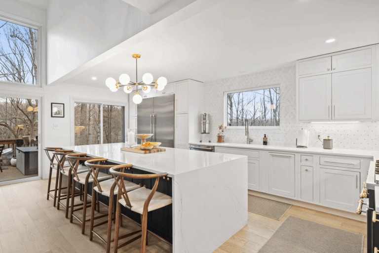 Bright transitional kitchen remodel in Northern Virginia by Veteran Built Homes featuring a waterfall-edge quartz island, white shaker cabinets, modern gold chandelier, stainless steel appliances, and wood-frame wishbone bar stools for a clean, contemporary look with natural light.