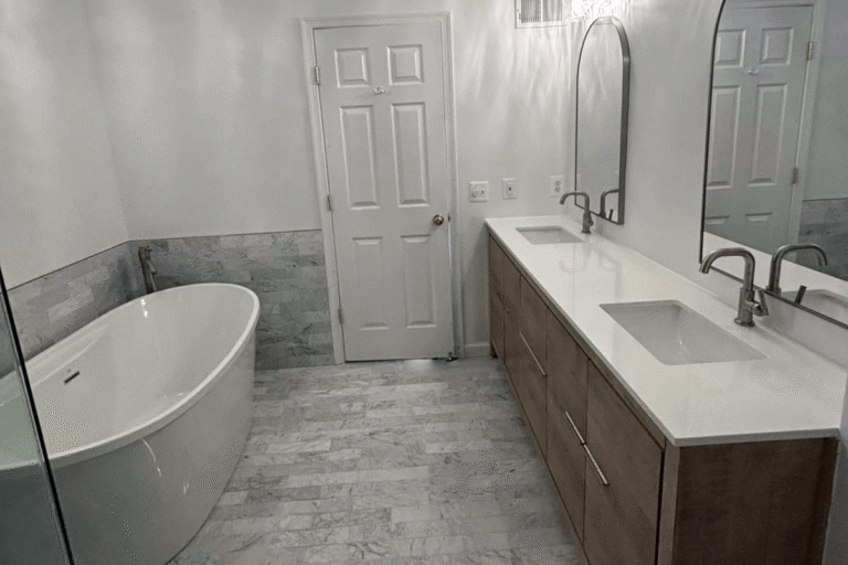Transitional bathroom remodel in Northern Virginia by Veteran Built Homes featuring a freestanding soaking tub, dual-sink wood vanity with white quartz countertop, arched mirrors, and marble-look tile flooring and wall accents for a clean and elegant design.