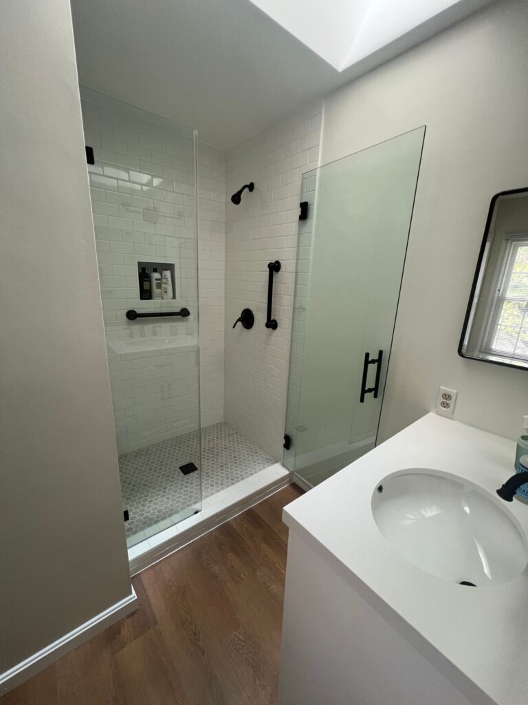 A modern bathroom with a glass shower door, sink, and handrails for enhanced safety.