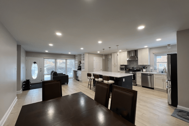 Open-concept kitchen and living area remodel in Northern Virginia by Veteran Built Homes, featuring a large central island with pendant lighting, white shaker cabinets, stainless steel appliances, luxury vinyl plank flooring, and custom built-in storage for a functional and stylish space.