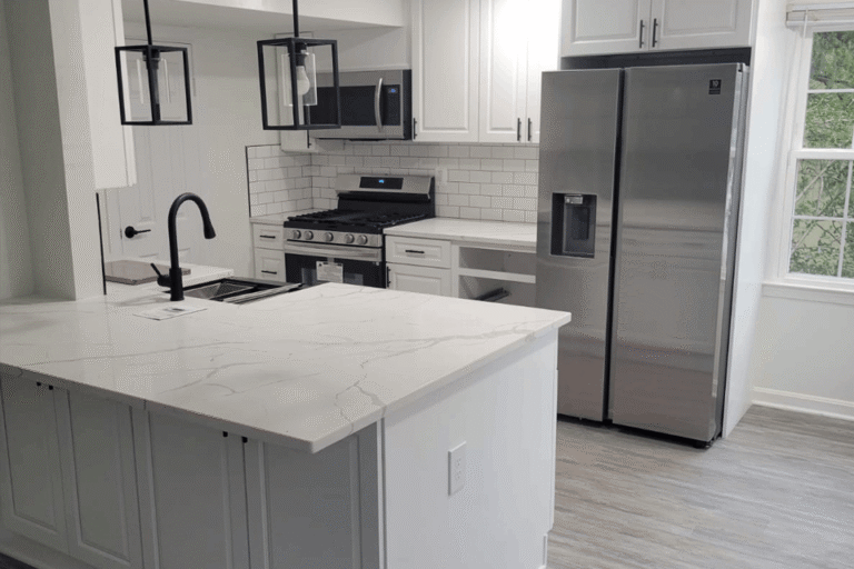 Modern kitchen remodel in Northern Virginia by Veteran Built Homes featuring white shaker cabinets, stainless steel appliances, subway tile backsplash, black hardware and fixtures, pendant lighting, and white quartz countertops with waterfall edge.