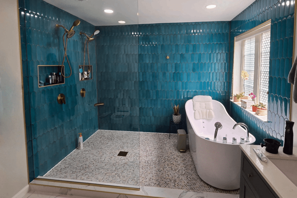 Luxurious bathroom remodel with walk-in shower featuring bold teal scallop tile, dual rainfall shower heads, built-in niches, and a freestanding soaking tub next to a sunlit window.