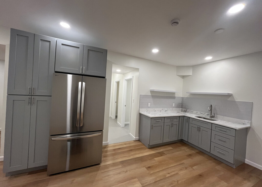 A basement kitchen featuring stainless steel appliances and warm wood floors.