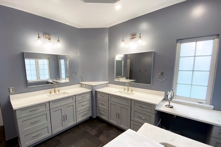 Master bathroom remodel at Fort Belvoir Virginia featuring dual separate gray shaker vanities with white quartz countertops, brushed gold faucets, frameless mirrors, matching vanity lighting, built-in makeup station with quartz countertop, and dark slate tile flooring by Veteran Built Homes