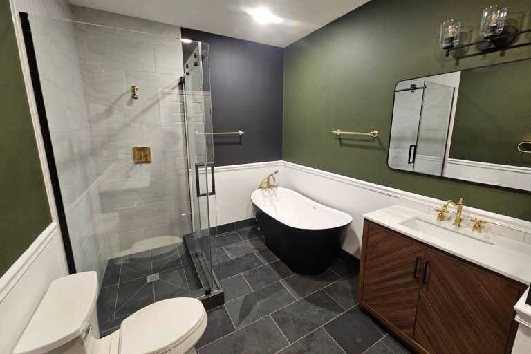 Luxury master bathroom remodel in Alexandria Virginia featuring frameless glass shower with marble-look tile, black freestanding soaking tub, brass fixtures, slate floor tile, and custom walnut vanity by Veteran Built Homes